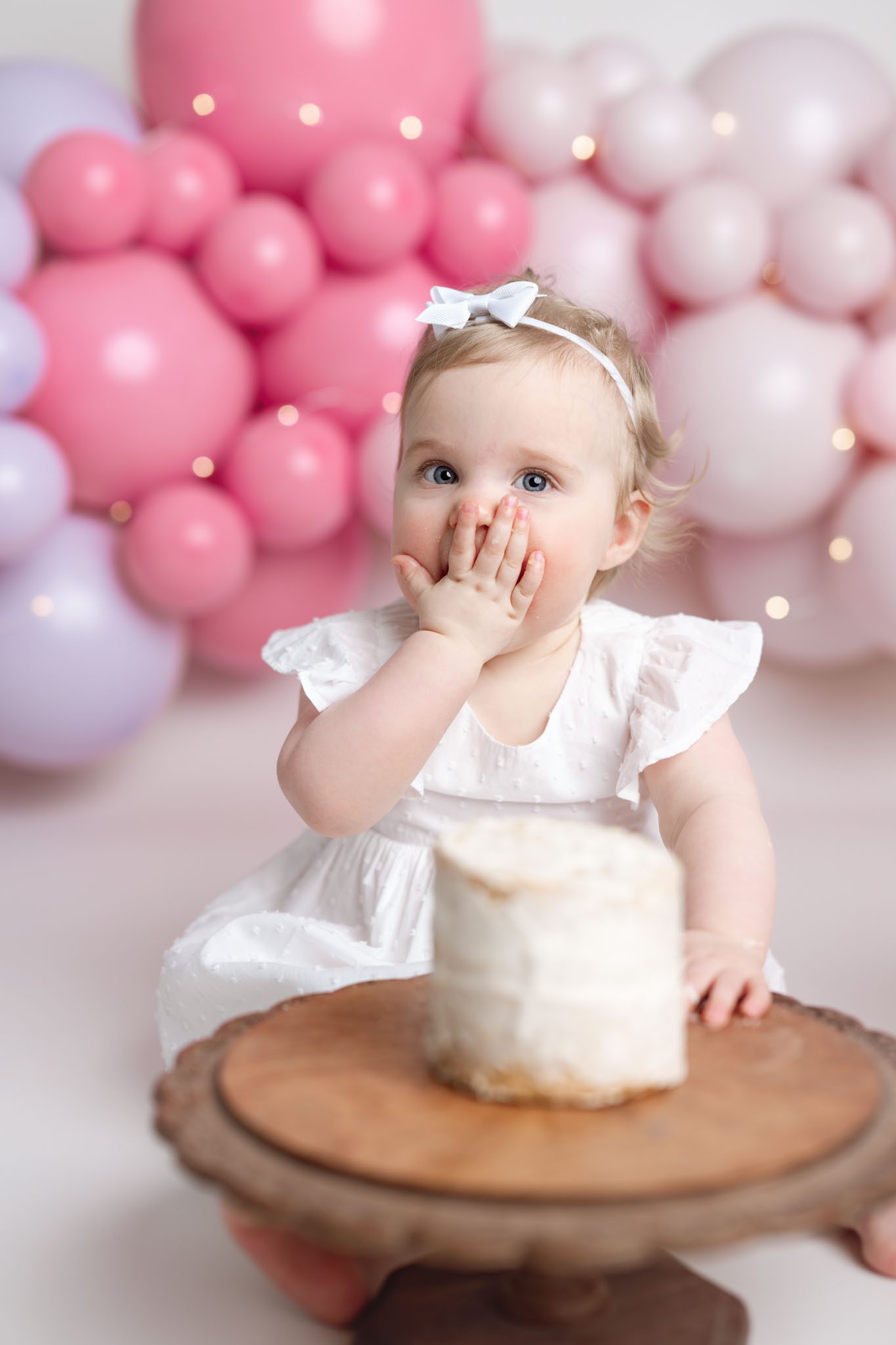 One twin girl covered in frosting happily eating a custom cake from V's Sweet Treats during her 1st birthday session.