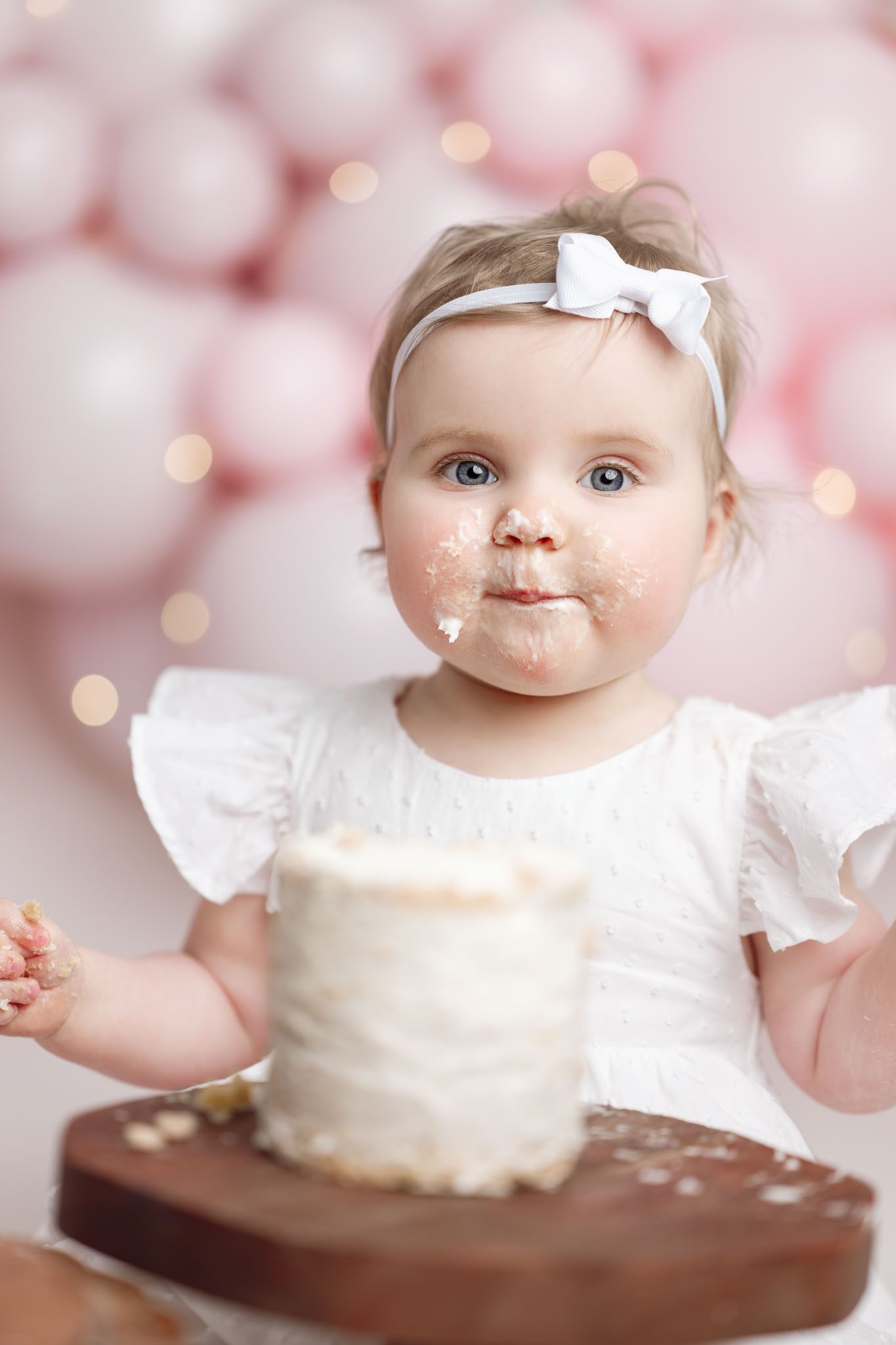 One twin girl covered in frosting happily eating a custom cake from V's Sweet Treats during her 1st birthday session.
