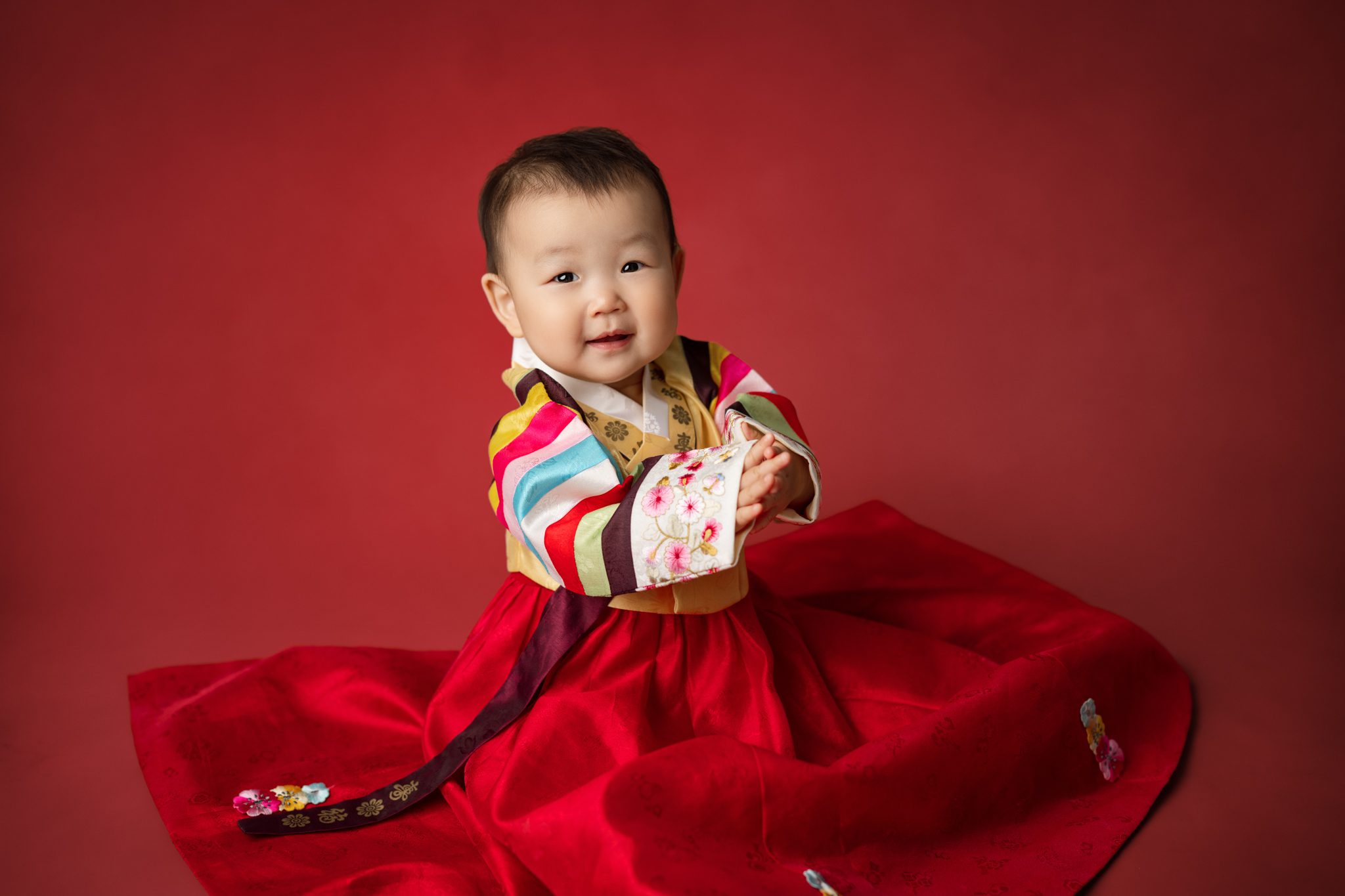 one year old baby girl on a red backdrop in a traditional Hanbok